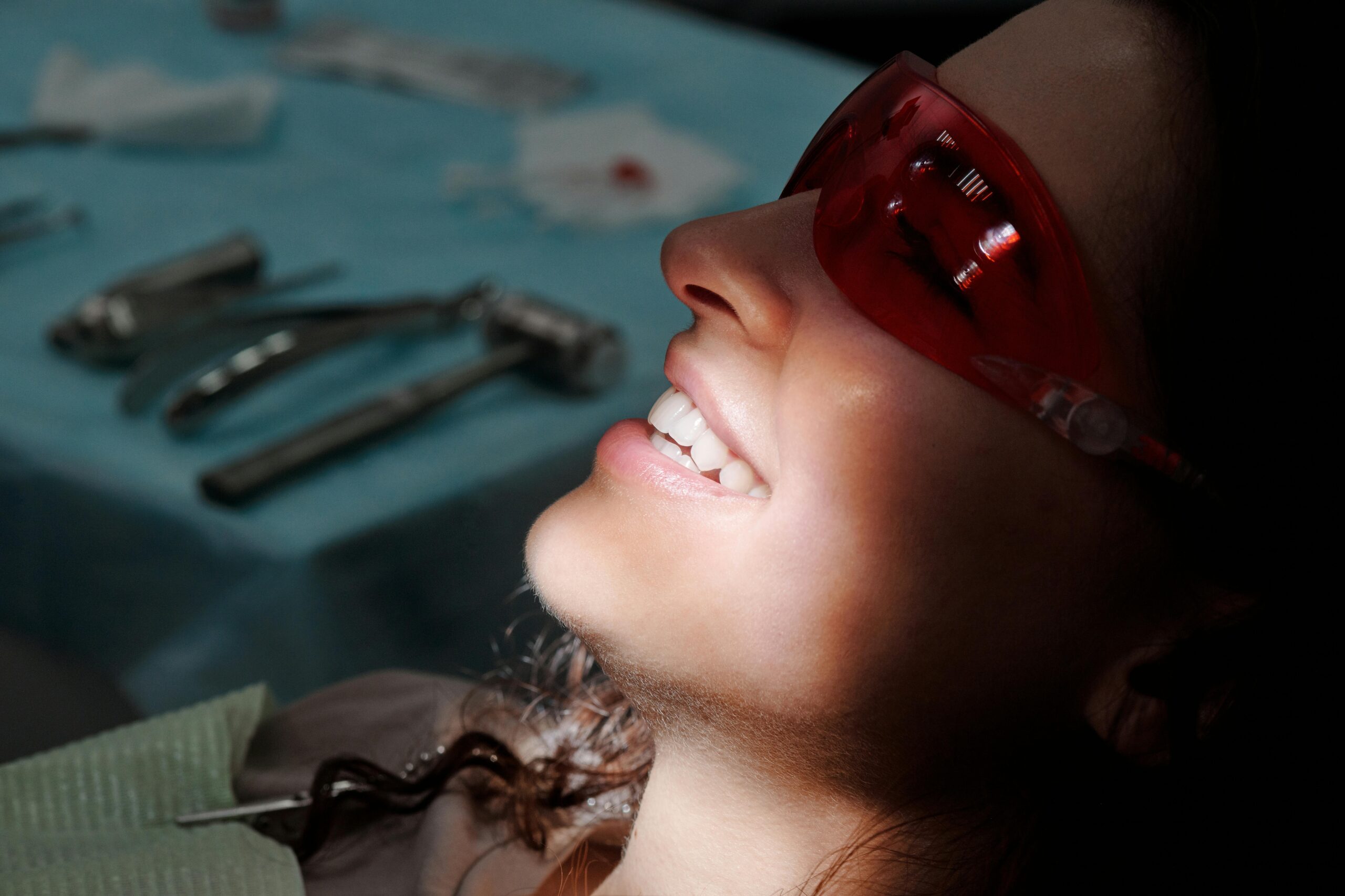 Close-up of a woman smiling with protective glasses at a dental clinic, highlighting her teeth.